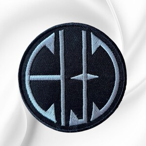 May include: A circular embroidered patch featuring a black background with a white stitched border and a central white monogram design. The design consists of two vertical lines intersected by horizontal elements forming the letters C, H, and J.