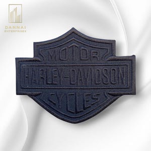 May include: A navy blue embroidered patch featuring the Harley-Davidson logo. The patch is shield-shaped with the words "MOTOR HARLEY-DAVIDSON CYCLES" stitched in a contrasting thread. The patch is likely for application on apparel or accessories.