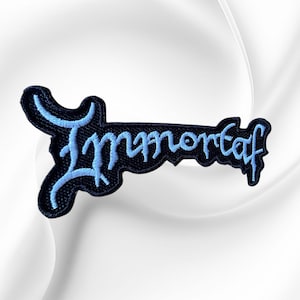 May include: An embroidered patch featuring the word Immortal in a stylized, jagged light blue font against a solid black background. The lettering has a distinct, sharp aesthetic with elongated strokes and a textured, stitched appearance throughout.