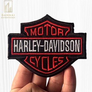 May include: A black, red, and white embroidered patch featuring the Harley-Davidson logo. The design includes the word MOTOR in red, HARLEY-DAVIDSON in white, and CYCLES in red, all set against a black background with a red border outline.