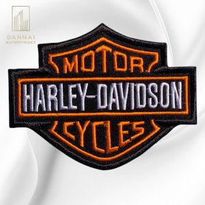 May include: A black embroidered patch featuring the Harley-Davidson logo. The design includes the word MOTOR in orange, the text HARLEY-DAVIDSON in white, and the word CYCLES in orange, all enclosed within a black shield-shaped border.