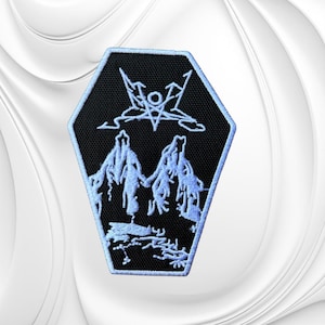 May include: A coffin-shaped embroidered patch with a black background and a light blue border. The design features a light blue embroidered pentagram symbol above two stylized mountain peaks and a rocky landscape at the base of the patch.