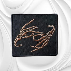 May include: A square black embroidered patch featuring a detailed design of two skeletal hands in a light brown thread. The hands are positioned facing each other with fingers slightly curved, creating a dark and intricate graphic on the fabric.