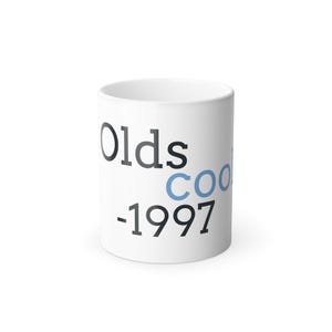 May include: White ceramic mug with the words "Olds Cool -1997" printed on the side. The word "Cool" is in a light blue color. The mug is cylindrical and has a handle.