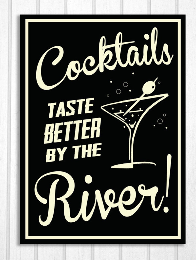 May include: Black and white sign with the text "Cocktails Taste Better By The River!" in a retro font. A martini glass with an olive is pictured next to the text.