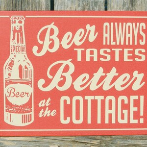 May include: Red wooden sign with white text that reads "Beer Always Tastes Better at the Cottage!"  A white outline of a beer bottle is on the left side of the sign.