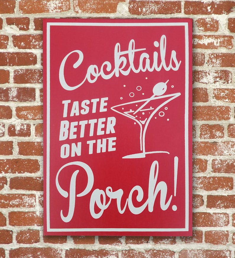 Op de afbeelding: Een rood houten bord met witte tekst die "Cocktails Taste Better On The Porch!" luidt, met een witte illustratie van een martini-glas met een olijf.