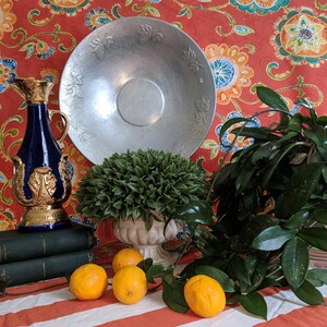Puede incluir: Un bodeg&oacute;n con una botella decorativa azul y dorada, una fuente de servir plateada, una planta verde en maceta y cuatro limones sobre un mantel a rayas rojas y blancas.