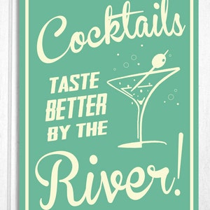 May include: A teal green sign with white text that reads "Cocktails Taste Better By The River!" with a white martini glass illustration.