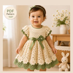 Könnte beinhalten: Ein cremefarbenes und salbeigrünes Häkelkleid mit rundem Ausschnitt, kurzen Rüschenärmeln und einem salbeigrünen Schleifenband mit passender Blumenapplikation. Der Rock hat einen gewellten Saum mit weißen Gänseblümchenmotiven und Perlen. PDF Pattern.
