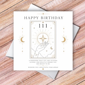 May include: A square greeting card featuring the text HAPPY BIRTHDAY at the top. The centre shows a rectangular tarot-style illustration of a hand holding a glowing star, the number 111, and crescent moons. Below is the text A REMINDER THAT YOU ARE ALIGNED, GUIDED, AND EXACTLY WHERE YOU ARE MEANT TO BE. WISHING YOU A BEAUTIFUL YEAR AHEAD.
