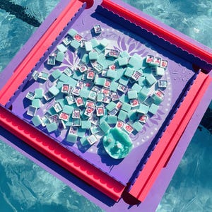 May include: A square purple and pink game board featuring a central circular area with a light purple floral pattern. Numerous small, light blue square tiles with various red and white graphic symbols are scattered across the board surface.