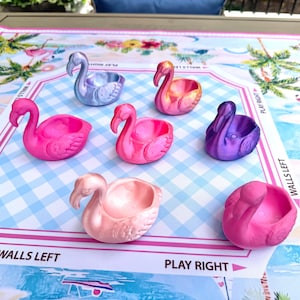 May include: Seven small flamingo-shaped bowls in various metallic and solid colors including light blue, orange, hot pink, purple, and pale pink. Each bowl features a sculpted flamingo head and neck with a hollow center for holding small items.