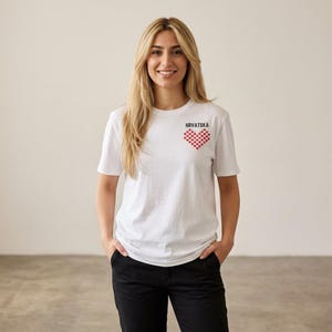 May include: A white short-sleeved t-shirt featuring a small red and white checkered heart graphic on the left chest. Above the heart, the word HRVATSKA is printed in black capital letters. The shirt has a crew neckline and a standard fit.