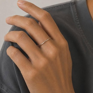 Op de afbeelding: Een dunne, gladde ring van zilverkleurig metaal die om de vinger wordt gedragen. De ring heeft een eenvoudig, rond ontwerp met een gepolijste afwerking. De tekst SM ESSENCE staat in het wit onderaan in het midden van het beeld.