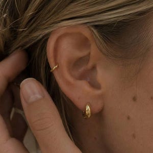 Könnte beinhalten: Nahaufnahme eines Ohrs mit goldenen Creolen und einem passenden Ohrklemme. Die Ohrringe sind klein und rund, glänzend. Der Text "SM ESSENCE" ist am unteren Bildrand zu sehen.