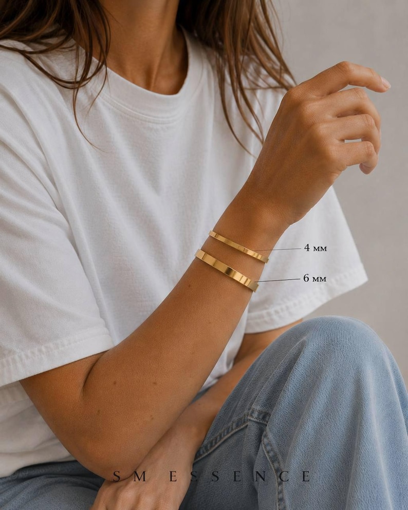May include: Gold-colored bracelets, 4 mm and 6 mm wide, are displayed on a person's wrist. The bracelets are simple, flat bands. The person is wearing a white t-shirt and blue jeans. The brand name "SMESSENCE" is visible at the bottom of the image.