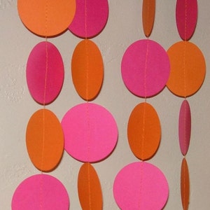 May include: A decorative garland featuring alternating orange and pink circles and ovals. The paper shapes are strung together with orange thread, creating a vibrant and playful design. The garland is suitable for party decorations or room decor.