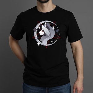 May include: A black short-sleeved t-shirt featuring a graphic print of a stylized grey wolf head in profile, positioned within a white crescent moon and a thin red pentagram, accented by several small four-pointed white and grey star shapes.