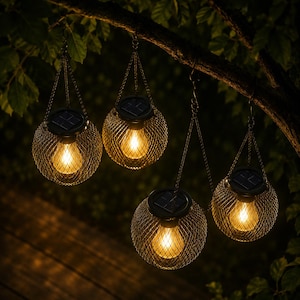 Op de afbeelding: Vier bolvormige zonnelantaarns met een donker metalen gaaskooi hangen aan een boomtak. Elke lantaarn is voorzien van een zonnepaneel aan de bovenkant, een warm gloeiende lamp in het draadframe en een dunne metalen ketting om op te hangen.