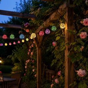 Op de afbeelding: Een lichtsnoer met bolvormige, veelkleurige ledlampen met een geperforeerd metalen ontwerp, hangend aan een houten pergola. De gloeiende bollen hebben verschillende kleuren, waaronder rood, blauw, groen, geel en paars, die de buitenruimte verlichten.
