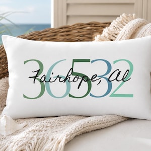 May include: A rectangular white throw pillow featuring the numbers 36532 in varying shades of green and blue. Overlaid across the center of the numbers is the text Fairhope, AL written in a black, handwritten-style script font.