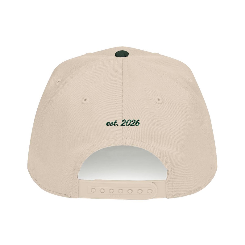 Puede incluir: Gorra de b&eacute;isbol beige con un bot&oacute;n verde oscuro en la parte superior. El texto "est. 2026" est&aacute; impreso en verde oscuro en la parte posterior de la gorra. La gorra tiene una correa ajustable.