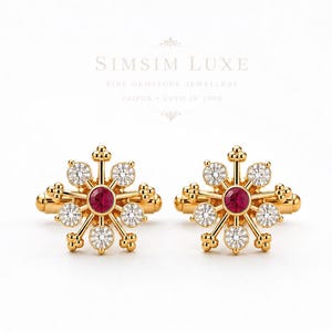 Könnte beinhalten: Ein Paar Manschettenknöpfe aus Gold mit einem zentralen runden roten Edelstein, umgeben von sechs kleineren klaren runden Edelsteinen in Sternform. Der Text SIMSIM LUXE FINE GEMSTONE JEWELLERY JAIPUR ESTD IN 1990 ist darüber zu sehen.