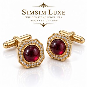 Op de afbeelding: Een paar gouden manchetknopen met een achthoekig frame, gezet met een dieprode edelsteen in cabochonslijpsel, omringd door een rand van kleine witte steentjes. De tekst SIMSIM LUXE FINE GEMSTONE JEWELLERY JAIPUR ESTD IN 1990 is zichtbaar.