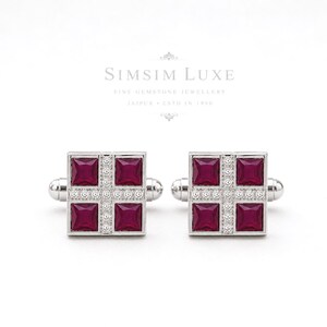 Puede incluir: Un par de gemelos plateados con diseño cuadrado, con cuatro rubíes de color rojo intenso en talla princesa dispuestos en forma de cruz, acentuados por pequeñas piedras claras a lo largo de las líneas centrales. El texto SIMSIM LUXE es visible.