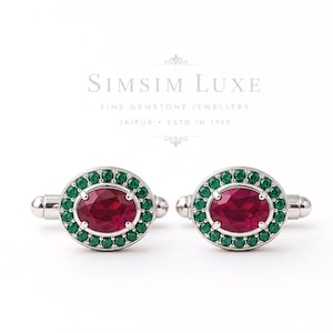 Op de afbeelding: Een paar zilveren manchetknopen met een centrale ovaal geslepen rode edelsteen omringd door een halo van kleine ronde groene edelstenen. Boven de manchetknopen staat de tekst SIMSIM LUXE FINE GEMSTONE JEWELLERY JAIPUR ESTD IN 1990.