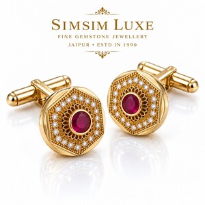 Könnte beinhalten: Ein Paar Manschettenknöpfe aus Gold mit sechseckigem Design, einem zentralen runden roten Rubin, umgeben von einem dekorativen Filigranmuster und einem Rand aus kleinen weißen Diamanten. Der Text SIMSIM LUXE FINE GEMSTONE JEWELLERY JAIPUR ESTD IN 1990 ist sichtbar.