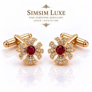 Könnte beinhalten: Ein Paar goldfarbene Manschettenknöpfe mit blumenförmigem Design, einem zentralen runden roten Edelstein und kleinen klaren Pavé-Steinen. Der Text SIMSIM LUXE FINE GEMSTONE JEWELLERY JAIPUR ESTD IN 1990 ist über den Manschettenknöpfen zu sehen.