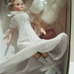 May include: A doll in a box, wearing a white textured dress and matching shoes with bows. The doll has blonde hair and a white veil. Additional white accessories are included. The doll is from the Narnia collection.