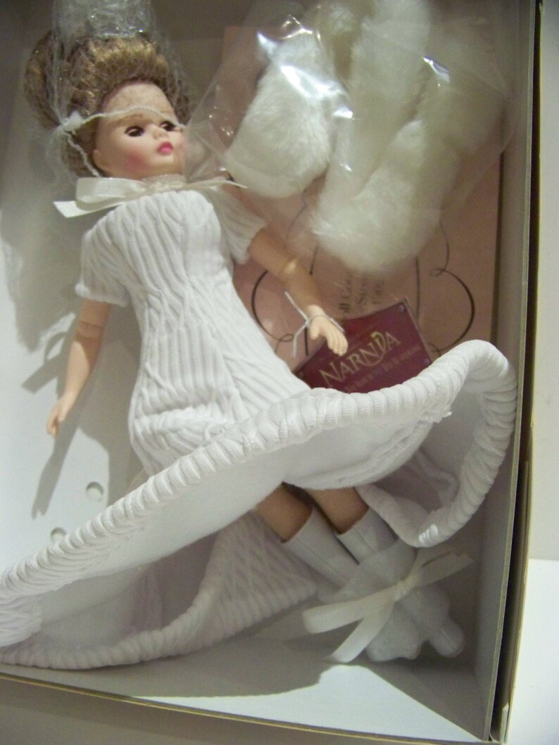 May include: A doll in a box, wearing a white textured dress and matching shoes with bows. The doll has blonde hair and a white veil. Additional white accessories are included. The doll is from the Narnia collection.