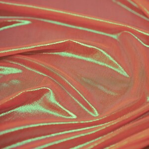 May include: A piece of fabric featuring a vibrant coral-orange base colour with a distinct iridescent sheen that reflects a bright lime-green light across the folds and creases of the material, creating a dynamic and shifting colour effect.