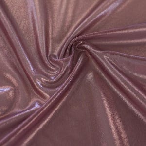 May include: A piece of fabric in a dusty rose colour with a metallic sheen. The material features a fine, textured knit surface that catches the light, creating deep folds and ripples across the surface that highlight the reflective quality.