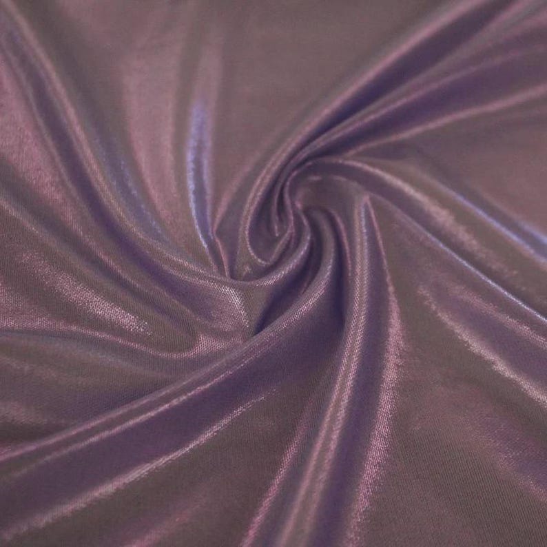 May include: A piece of fabric in a deep shade of lavender purple with a smooth, reflective, and metallic sheen. The material is draped in soft, flowing folds that create varying light and shadow patterns across the surface of the textile.