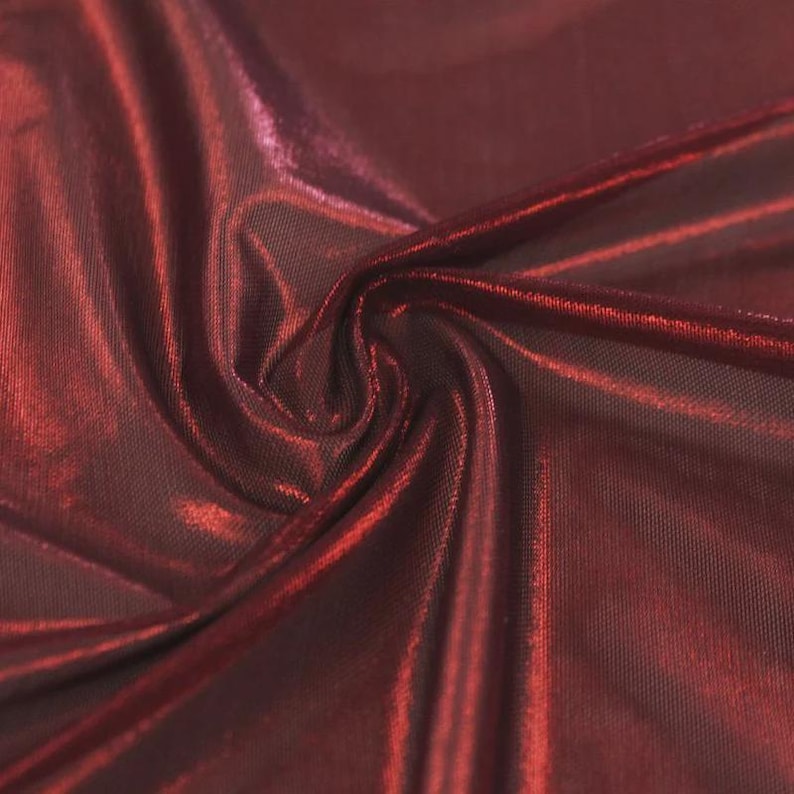 May include: A deep burgundy fabric with a metallic, reflective sheen. The material features a fine, mesh-like texture visible beneath the glossy surface, with soft folds and drapes creating varied light and shadow across the dark red surface.