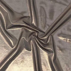 May include: A metallic bronze fabric with a shimmering, reflective surface. The material is draped in soft folds, creating deep shadows and bright highlights that emphasise the smooth, lustrous texture and the warm, golden-brown colour tones.