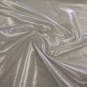 May include: A piece of silver-coloured fabric with a high-gloss, metallic finish. The material is draped in soft, flowing folds, creating deep shadows and bright highlights across the smooth, reflective surface of the textile material.