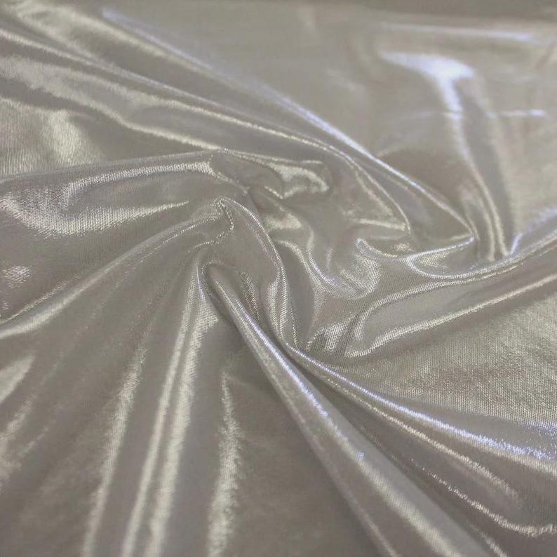 May include: A piece of silver-coloured fabric with a high-gloss, metallic finish. The material is draped in soft, flowing folds, creating deep shadows and bright highlights across the smooth, reflective surface of the textile material.