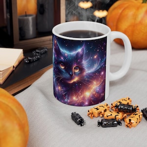 May include: White ceramic mug featuring a vibrant illustration of a cat with a galaxy design. The cat's fur is depicted with swirling blues, purples, and oranges, with sparkling stars. The mug is filled with dark liquid, possibly coffee or tea.