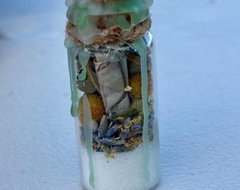 Peut inclure: Petite bouteille en verre remplie de granules blancs, de fleurs séchées et d'herbes. La bouteille est scellée avec un dessus décoratif et une bande de ficelle naturelle. De la cire verte coule sur les côtés de la bouteille.