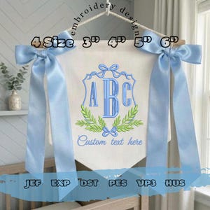 May include: A white banner with a blue monogram and the text "Custom text here." The banner is decorated with blue bows and ribbons. The banner is 7.6, 10.2, 12.7, and 15.2 cm wide.