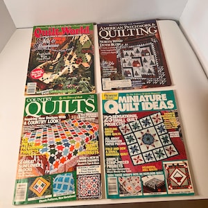 May include: Four vintage quilting magazines are displayed, showcasing colorful quilt patterns and designs. Titles include "Quilt World," "American Patchwork & Quilting," "Country Quilts," and "Miniature Quilt Ideas." The magazines feature various quilting projects and techniques.