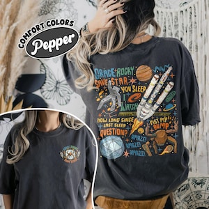 May include: A charcoal gray t-shirt featuring a space-themed graphic on the back and a smaller matching logo on the front. The back design includes a rocket, an astronaut, a planet, and text that reads Grace Rocky Save Star You Sleep I Watch.