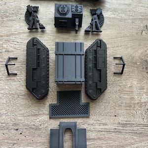 May include: A collection of unassembled matte black plastic model tank parts, including a long main cannon, two track assemblies, a central hull section, a turret component, two side supports, a mesh floor plate, and a curved front armor piece.