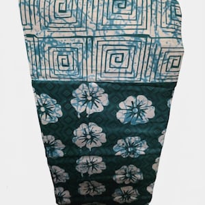 May include: A fabric textile featuring two distinct sections. The top portion displays a white background with a blue geometric square pattern. The bottom portion features a dark teal background with a repeating pattern of light blue floral shapes.