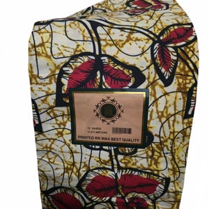 May include: A folded bolt of fabric featuring a cream background with a repeating pattern of black branches and red leaves. A rectangular label is attached, reading 12 YARDS, 10.972 METERS, and PRINTED RR WAX BEST QUALITY with a circular logo.